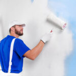 A painting contractor using a roller to paint a wall in a residential setting.